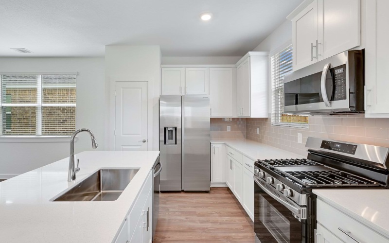 An interior view of a kitchen with kitchen cabinetry, a kitchen sink, a closet pantry door, a large window, and stainless steel appliances including a fridge, oven, microwave, and stovetop at Katy Legacy houses in Katy, TX