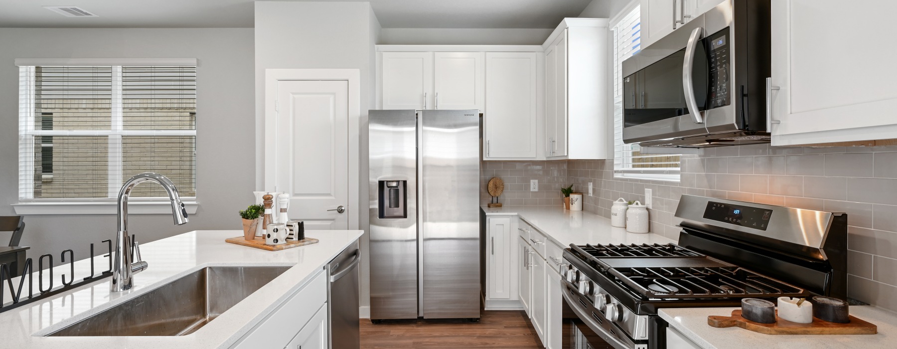 An interior view of a kitchen with kitchen cabinetry, a kitchen sink, a closet pantry door, a large window, and stainless steel appliances including a fridge, oven, microwave, and stovetop at Katy Legacy homes in Katy, TX